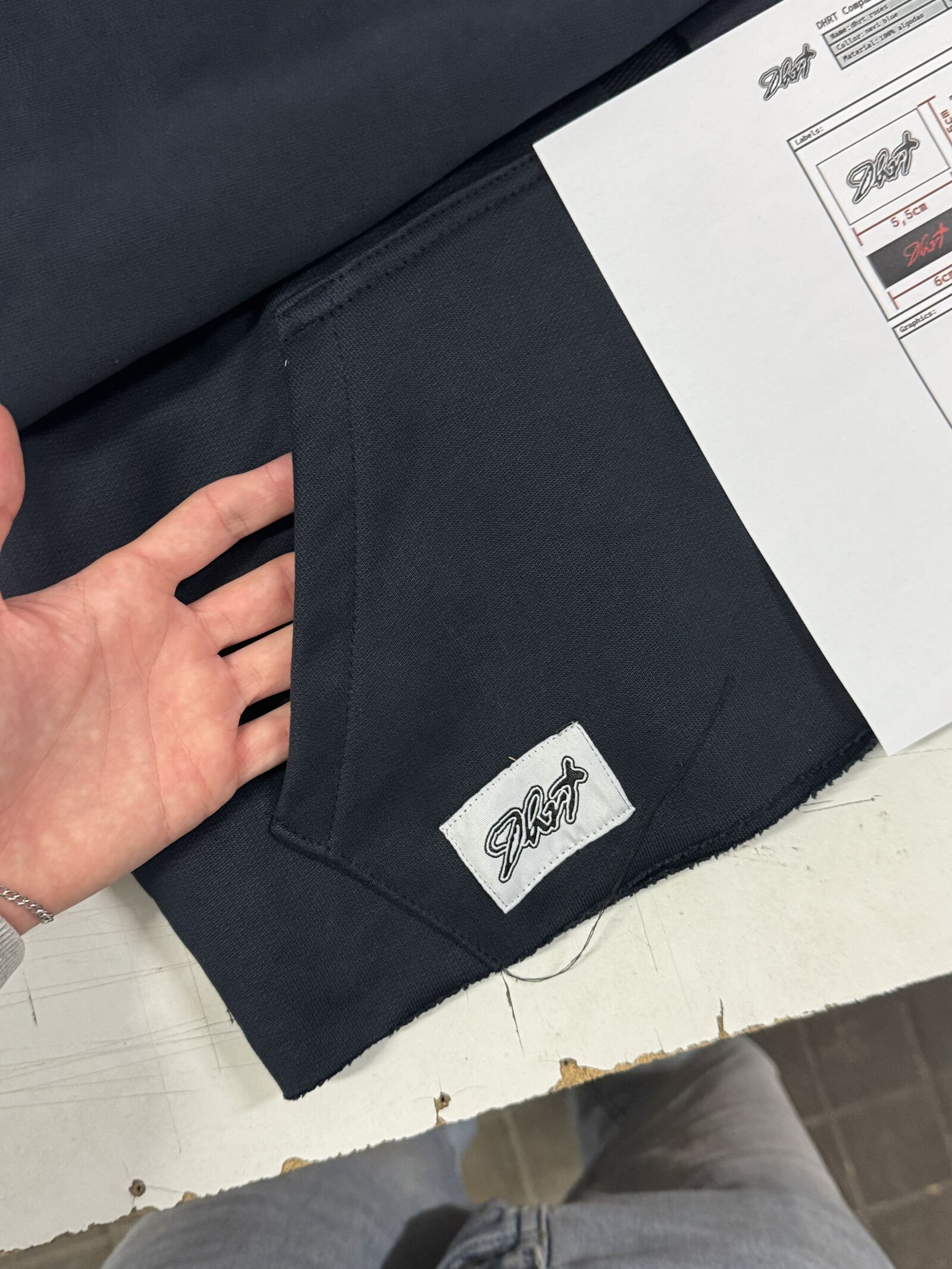 Worker inspecting dark navy fabric with woven brand label and technical spec sheet
